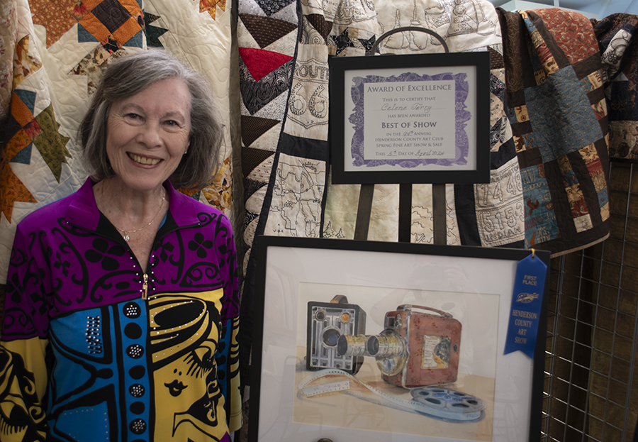 Photo of Best of Show winner Celene Terry standing next to her painting in front of a backdrop of quilts.